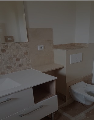 Aménagement Salle de Bain : WC, Meuble et Mosaïque Salle de bain moderne en rénovation avec meuble-lavabo blanc, mosaïque beige et WC suspendu en attente d'installation. Prise murale visible.