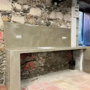 Comptoir de cuisine en béton ciré brut sur mur de pierres apparentes, installation électrique en cours. Prises visibles.