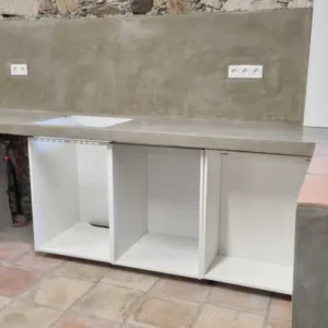Installation cuisine en cours : meubles bas blancs sans portes sous plan de travail béton, évier encastré, prises électriques murales visibles.