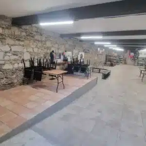 Salle rustique avec mur en pierre, plancher surélevé carrelé et tables pliantes empilées, préparation pour événement.