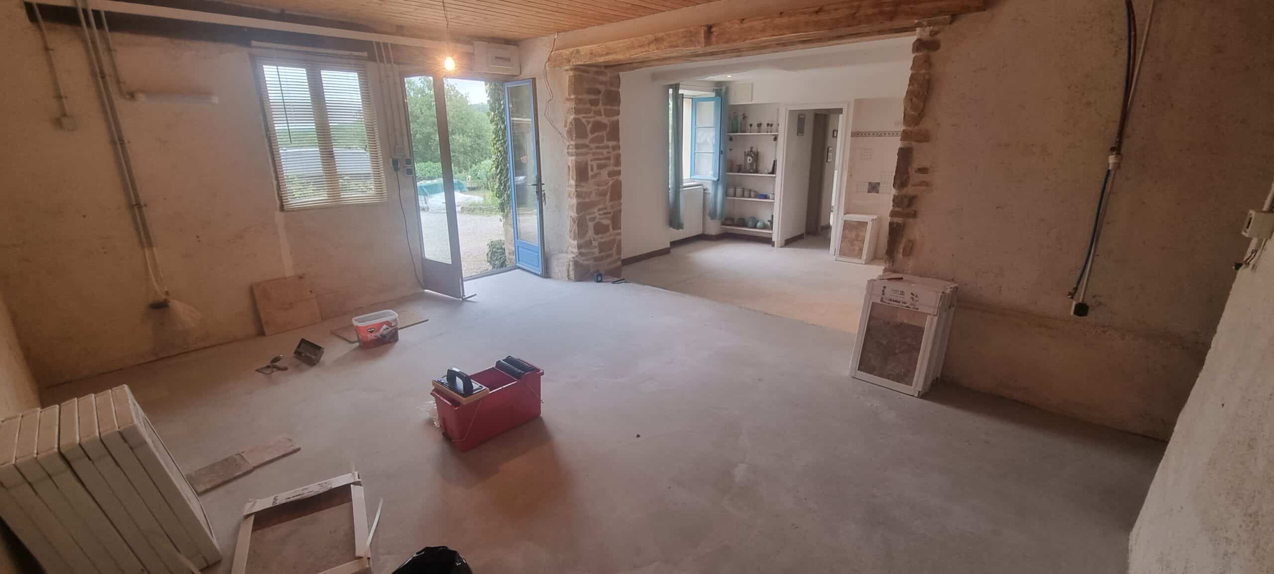 Intérieur rustique en rénovation avec sol en béton, une porte bleue ouverte, outils de maçonnerie et matériaux de carrelage.