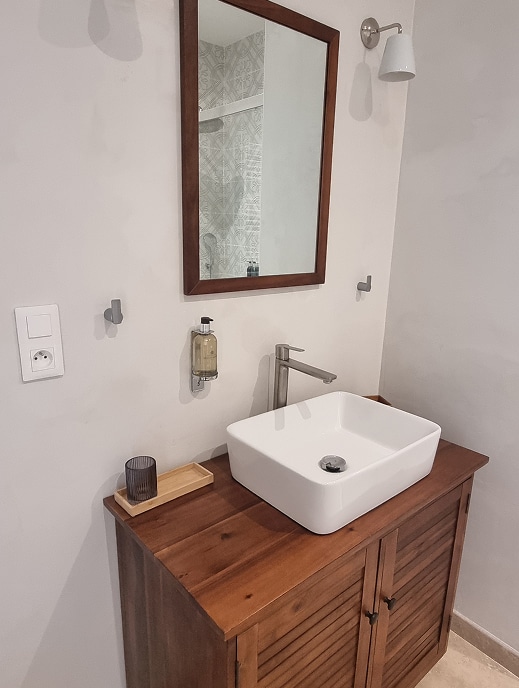 Meuble vasque bois, lavabo moderne et miroir salle de bain Salle de bain moderne avec meuble vasque en bois, lavabo carré blanc posé, miroir encadré et applique murale. Prise électrique visible.